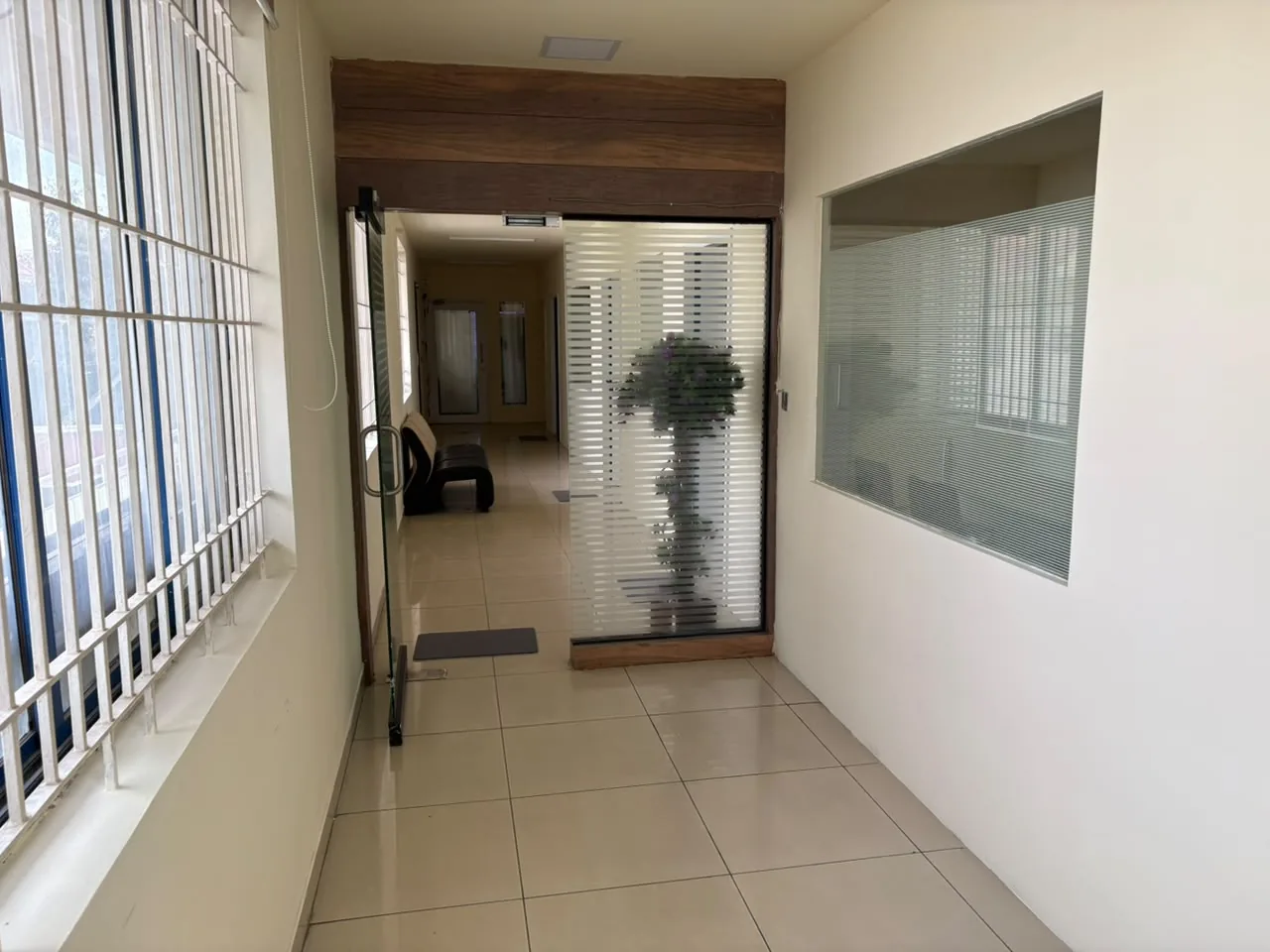 A passage with barred windows on the left leading to an open glass door and a frosted glass partition, with the corridor visible beyond.