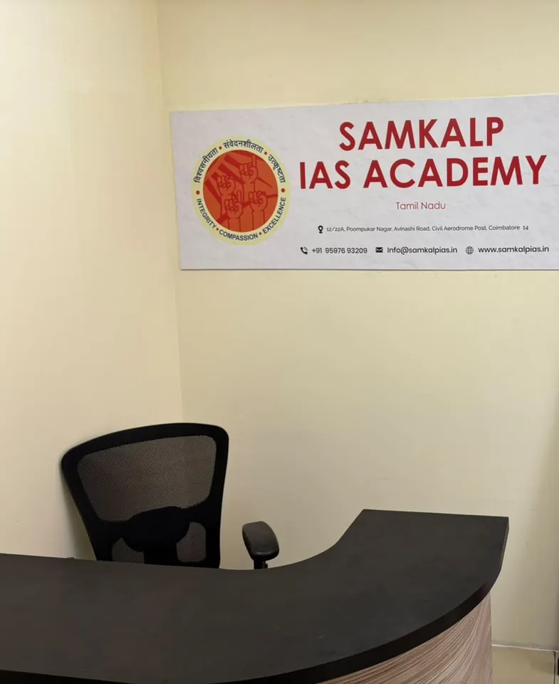 A dark curved reception desk and an office chair beneath a white Samkalp IAS Academy wall sign.